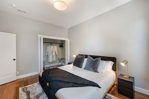 Une chambre à coucher comprenant un lit, des tables de chevet, une commode, un placard et un luminaire au plafond.