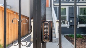 A metal gate with a keypad lock, a wooden fence, and a staircase leading to a building. - / Luxury Modern Home in Oakland with AC & WFH / (Oakland)
