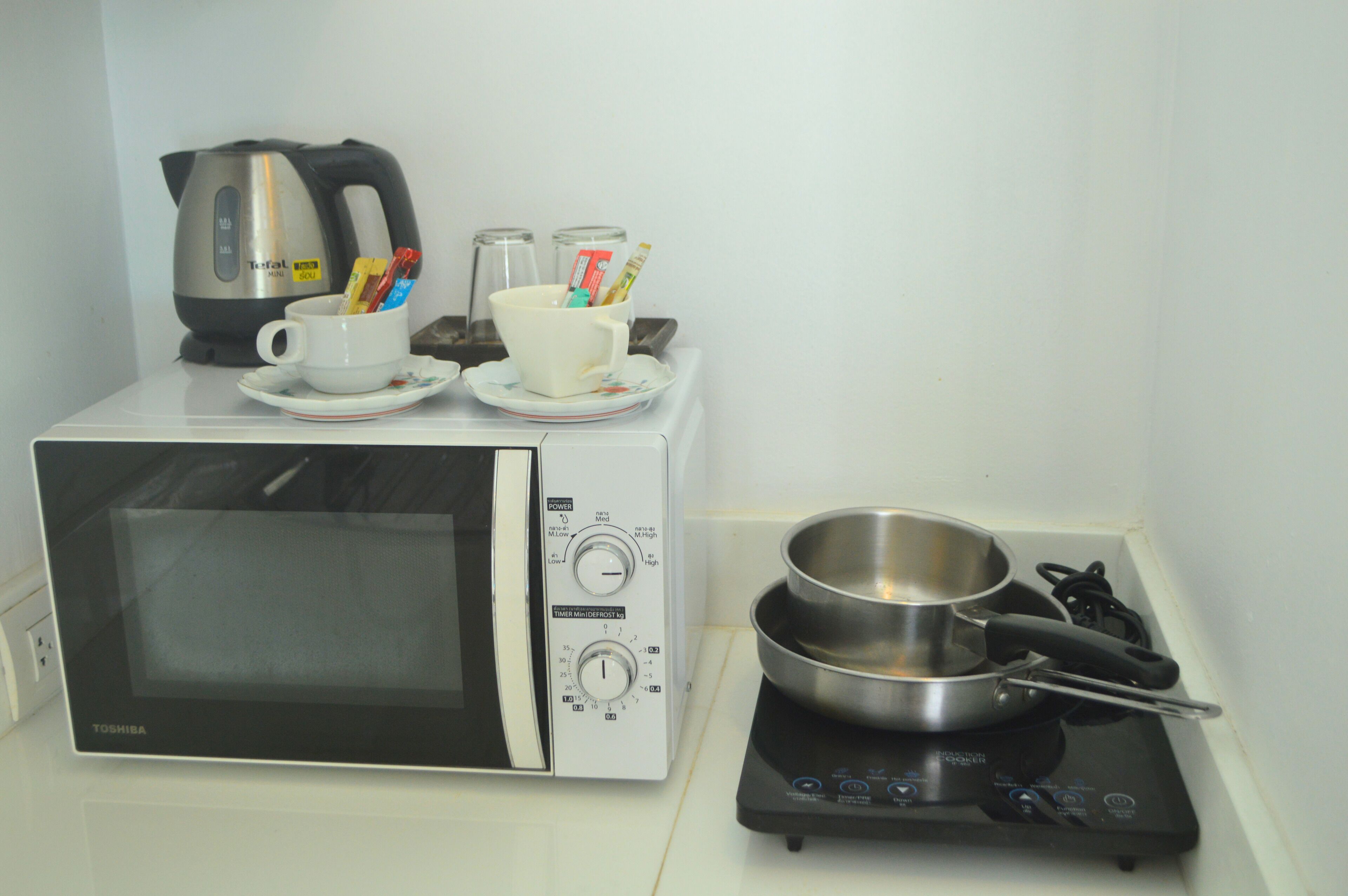 Une cuisine équipée d’un four à micro-ondes, d’une bouilloire, d’une tasse avec des couverts et d’une poêle sur une plaque de cuisson mobile.