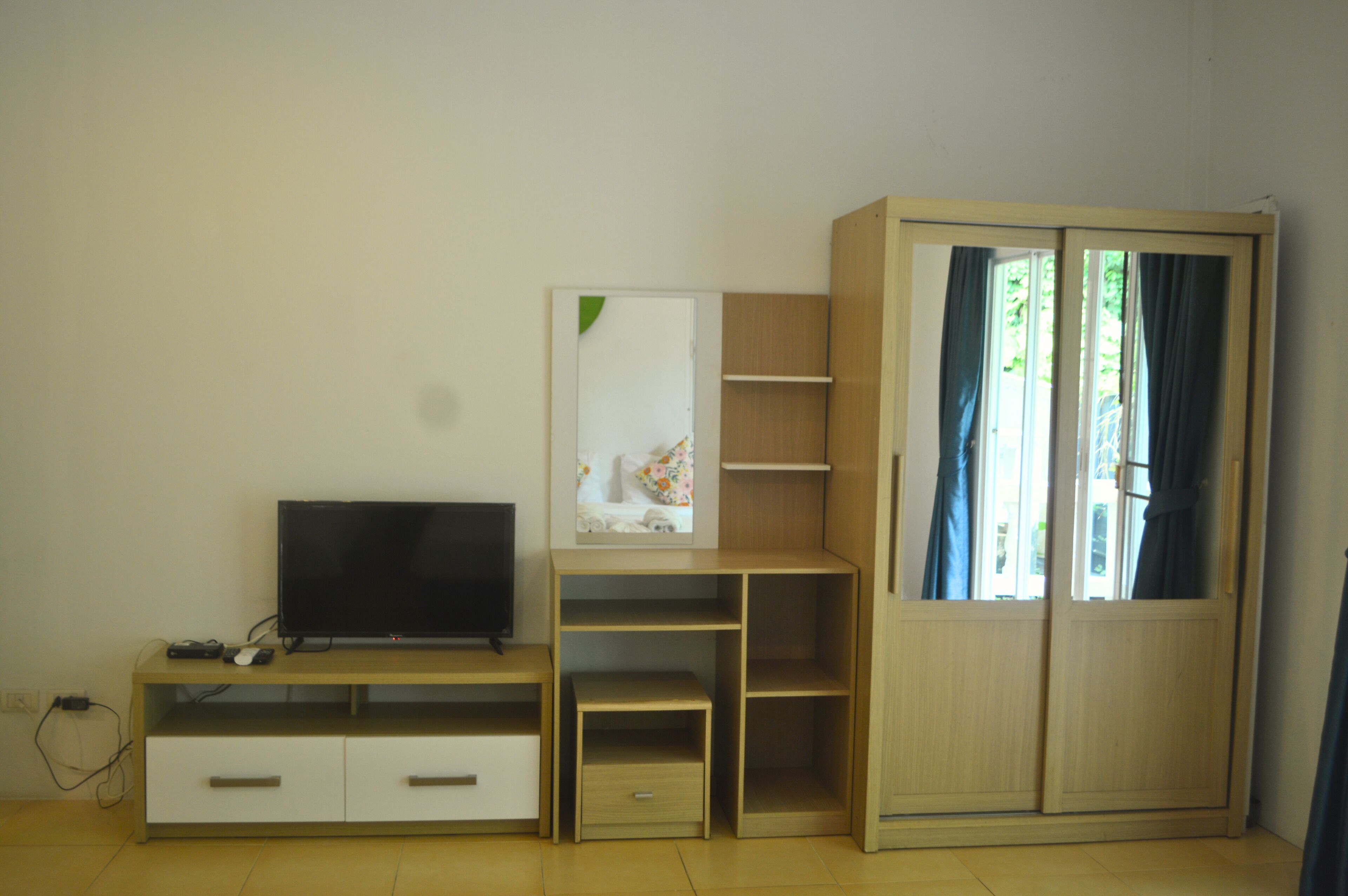 Una habitación con televisión, un armario de madera con estantes y un escritorio pequeño.