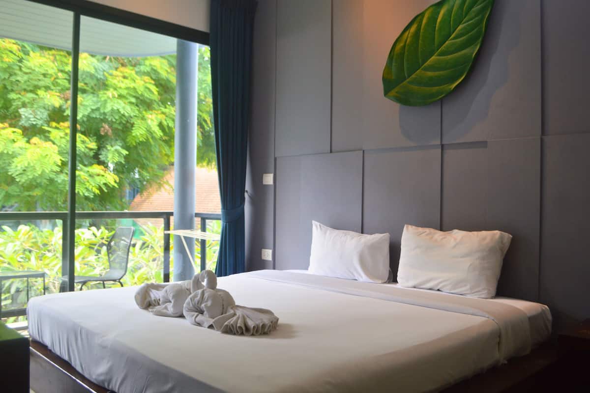 A hotel room with a large bed, a view of greenery outside, and a leaf decoration on the wall.
