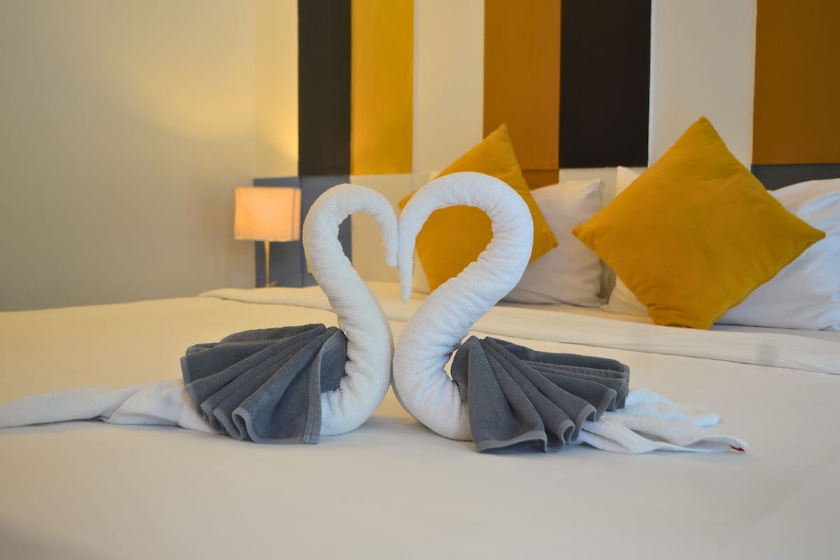 A bed with a heart-shaped towel arrangement and a yellow pillow.