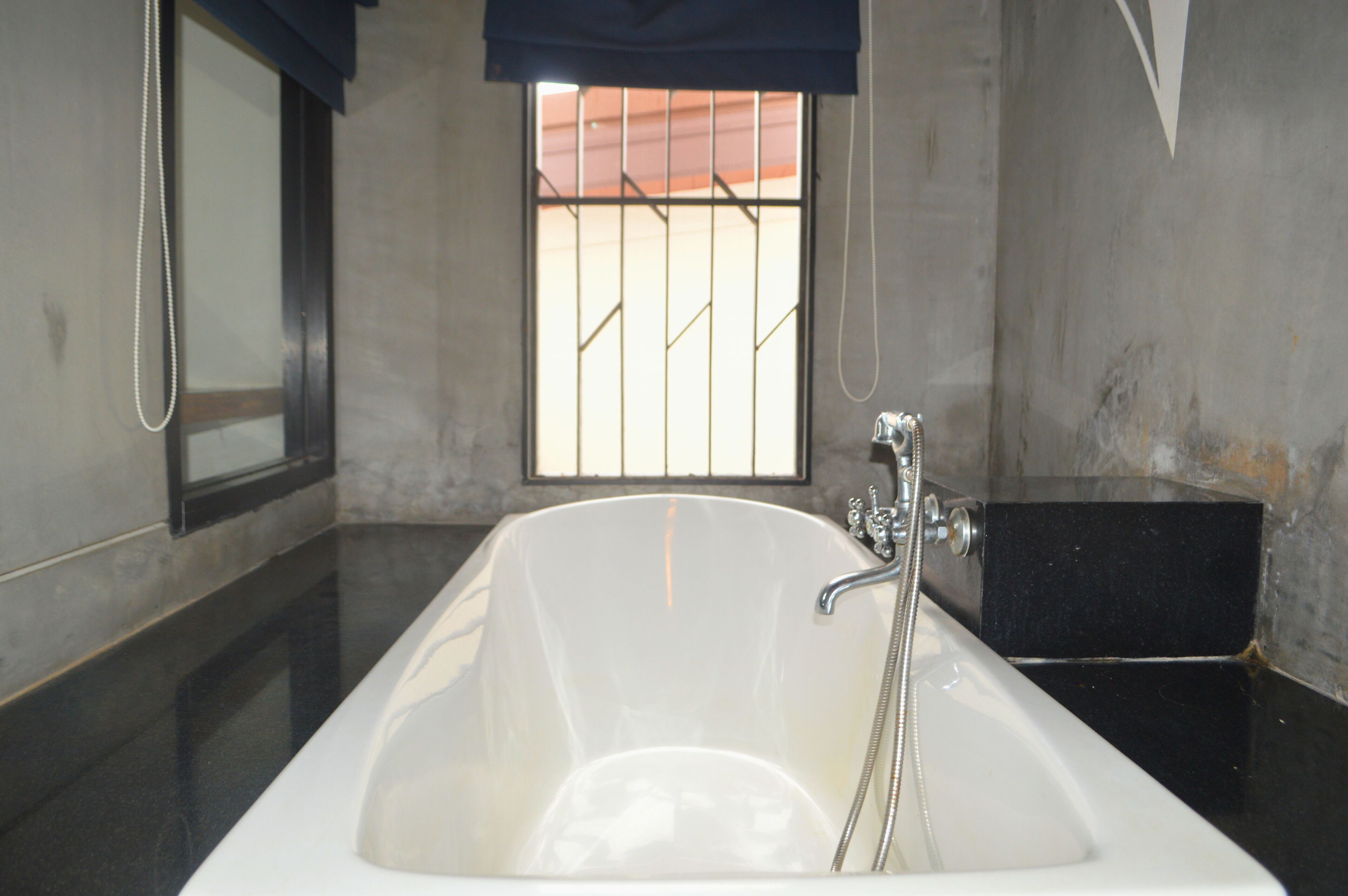 Un baño con bañera, una ventana con barrotes y una ducha.
