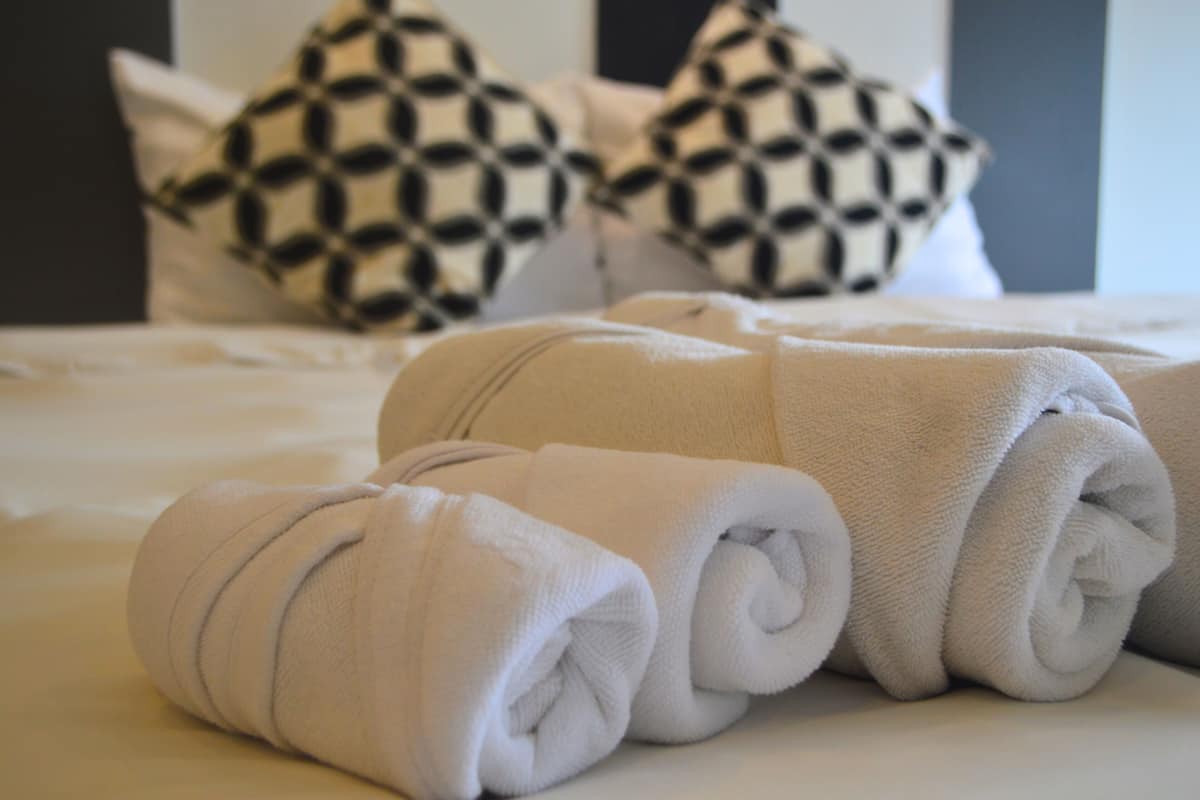 A neatly made bed with rolled white towels and patterned pillows.