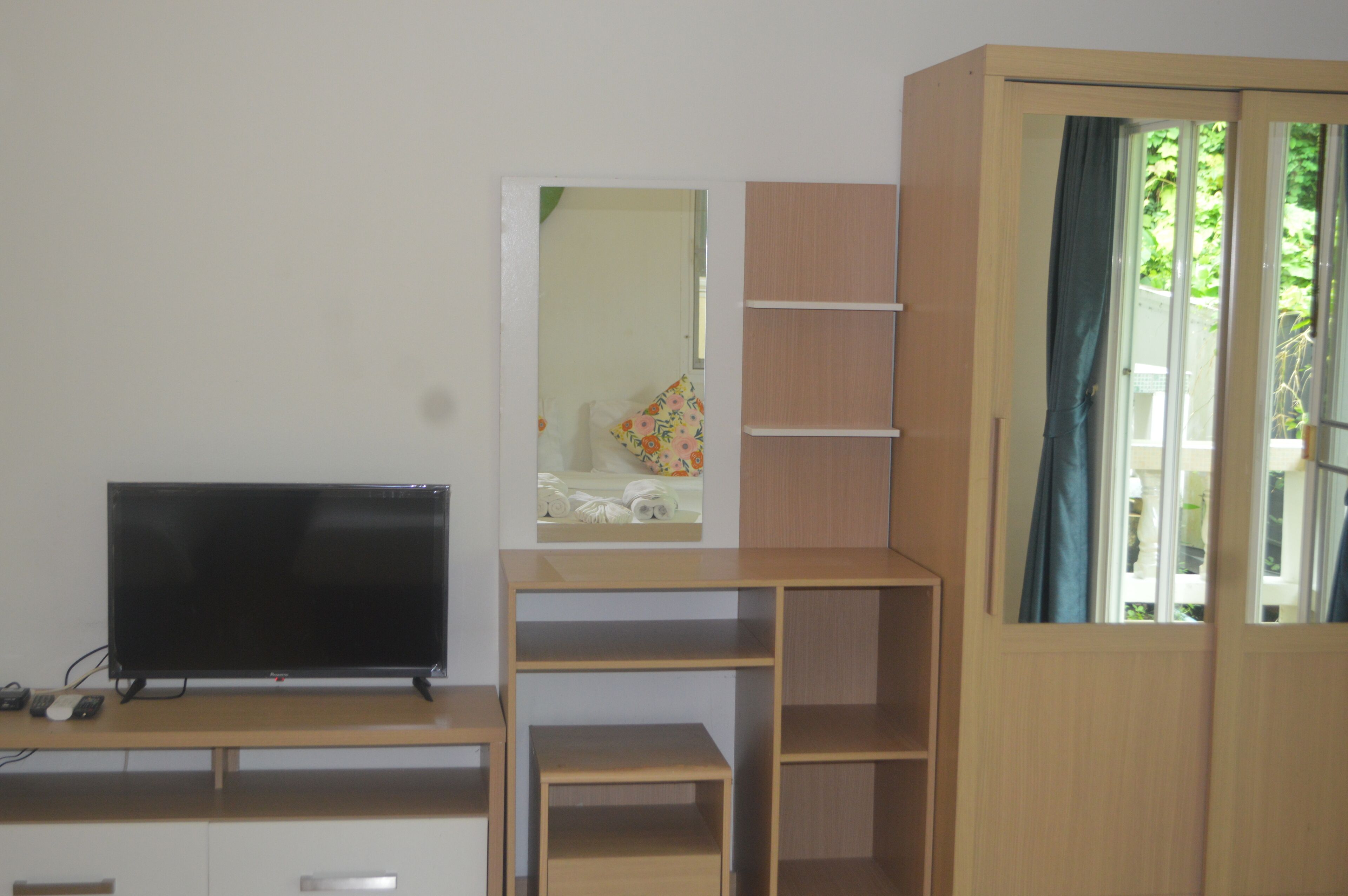 A room with a television on a wooden stand, a mirror, and a wardrobe with a window.