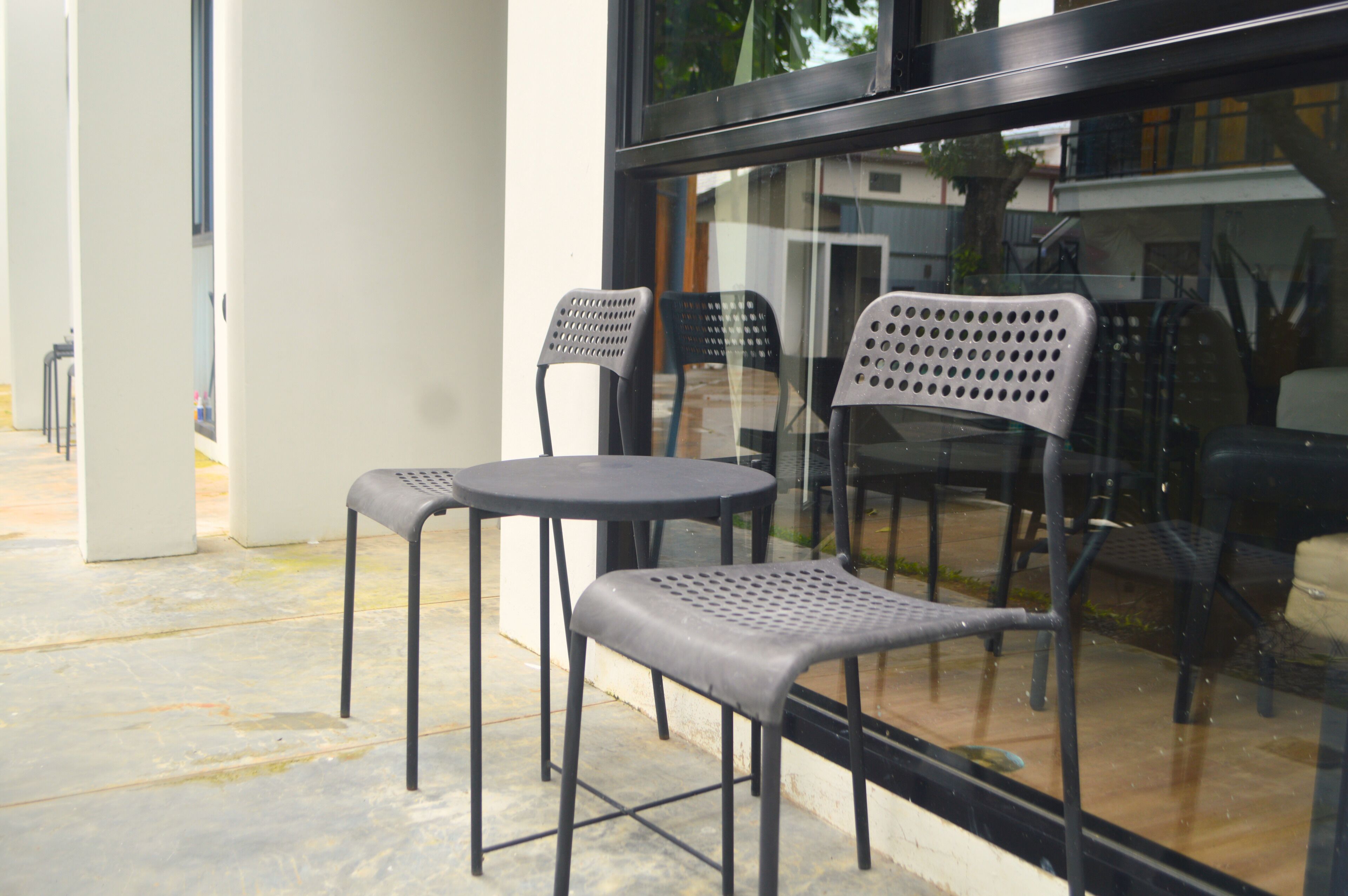A modern outdoor seating area with two round tables and four chairs, featuring a glass partition and a view of the surrounding area.