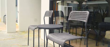 A modern outdoor seating area with two round tables and four chairs, featuring a glass partition and a view of the surrounding area.