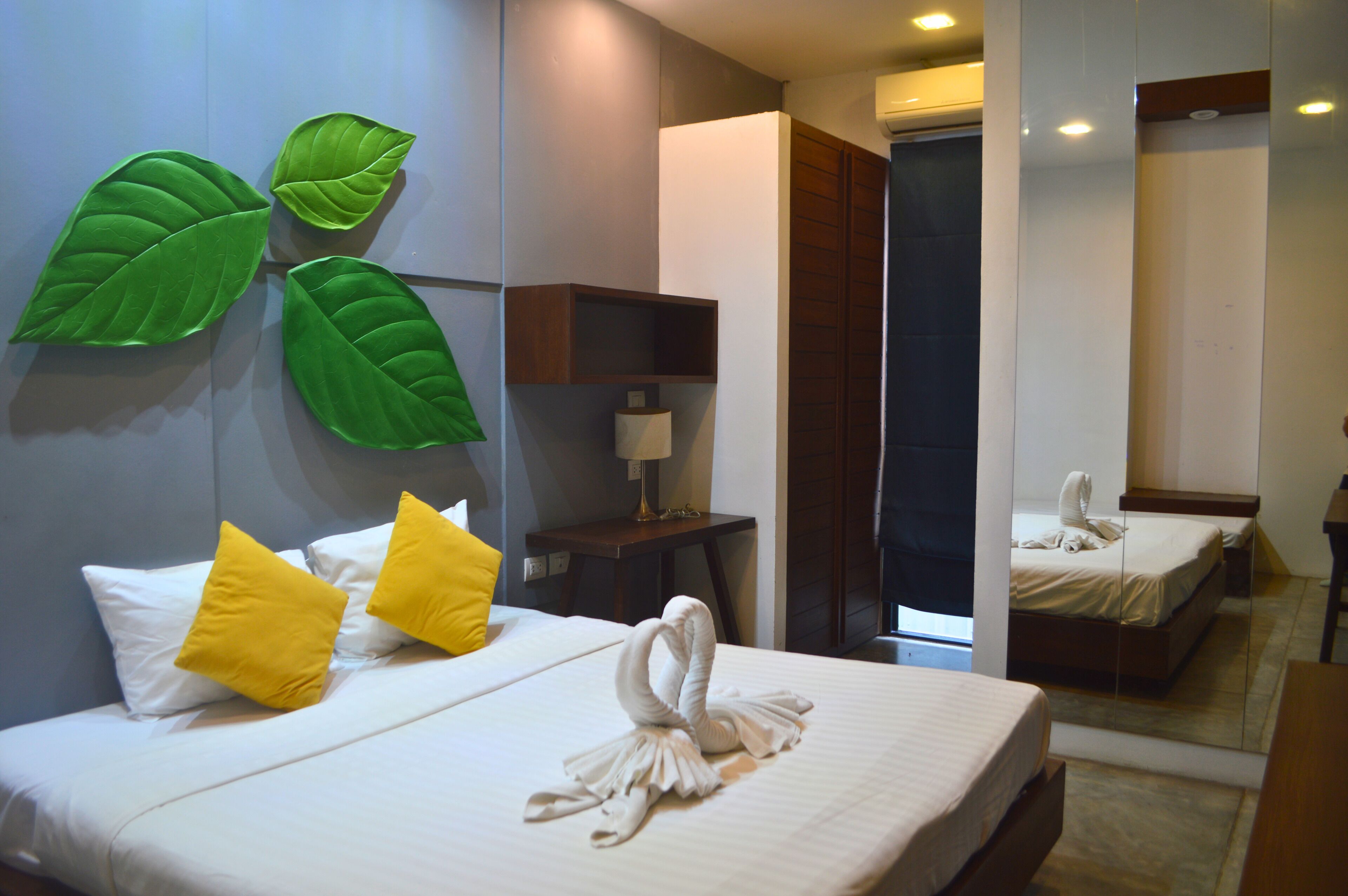 A hotel room with a bed, pillows, a mirror, and a wall with green leaf decorations.