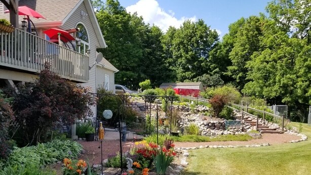 A residential property with a well-maintained garden, a wooden deck with red umbrellas, and a stone pathway leading to a gazebo. - 3 miles from Sunburst Ski Hill. Close to  great hikiing and snow mobile trails (Kewaskum)
