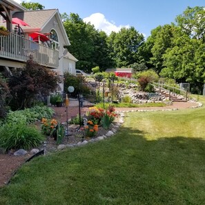 Il s'agit d'une propriété résidentielle dotée d'un jardin bien entretenu, d'une terrasse en bois agrémentée de parasols rouges et d'un chemin de pierre menant à un belvédère.