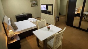 A hotel room with a bed, bedside table with a lamp, a small table with a flower, a chair, a desk, and a wardrobe. - Continental Hotel Baku (Baku)