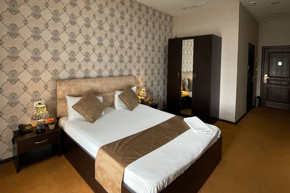 Une chambre d’hôtel avec un grand lit, une armoire, une table de chevet avec une lampe et un miroir.
