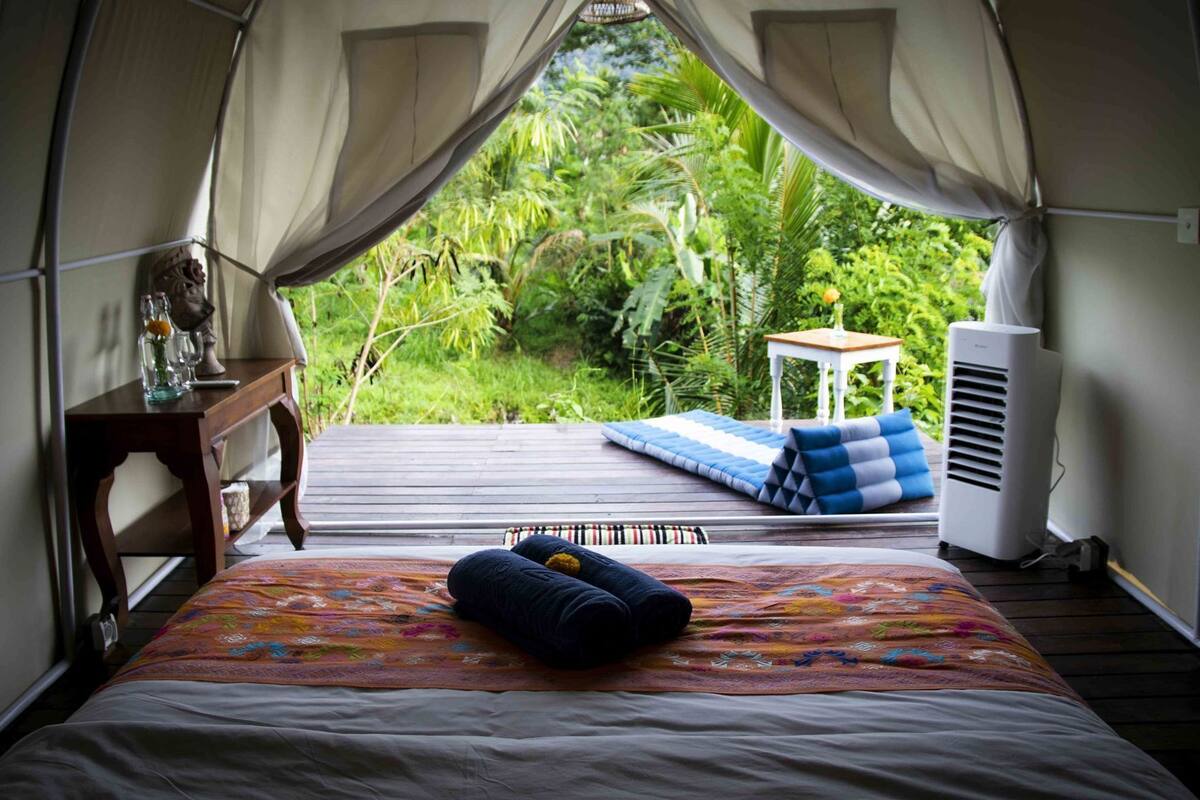 A tented room with a bed, pillows, a small table, and a heater.