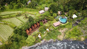 Vista aérea de un resort tropical con cabañas de techo de paja, una piscina y campos en terrazas.