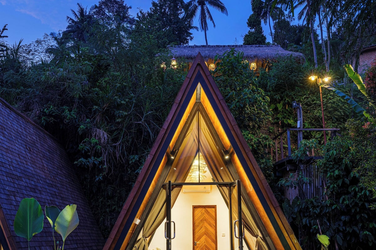 A triangular-shaped tent-like structure with a wooden deck and a door leading inside.