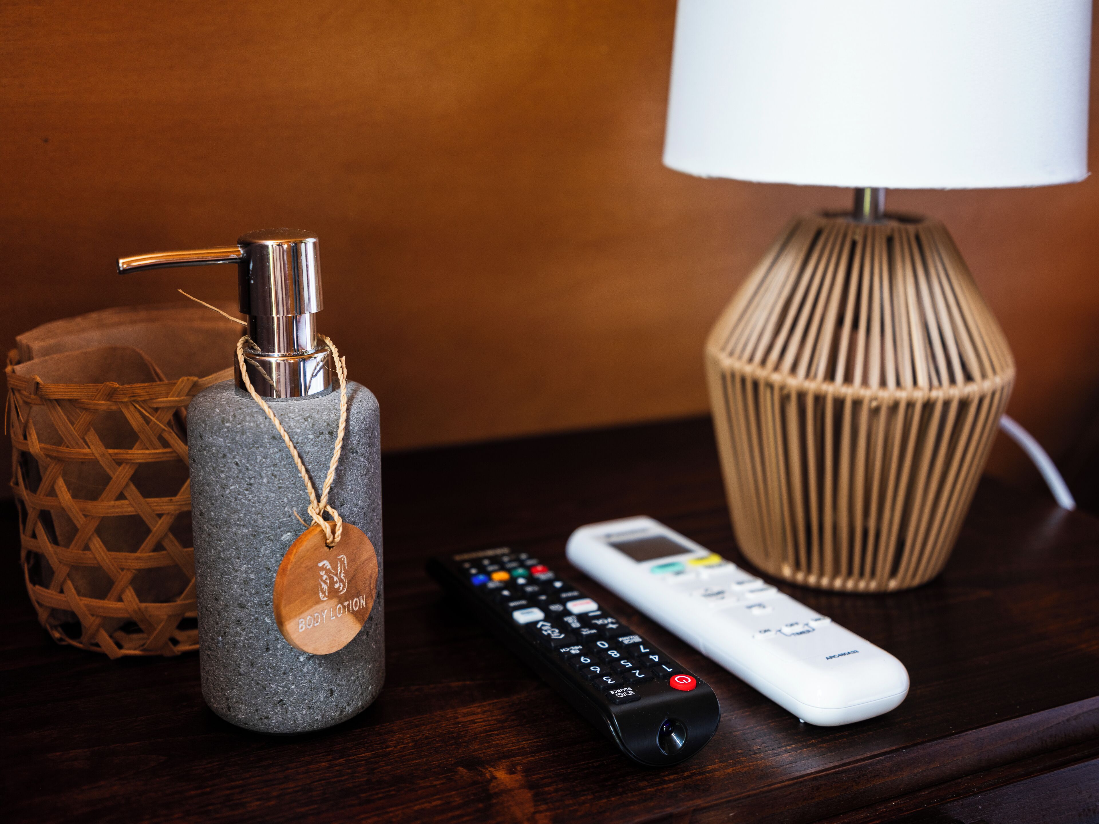 A remote control, a body lotion dispenser, and a lamp on a wooden surface.