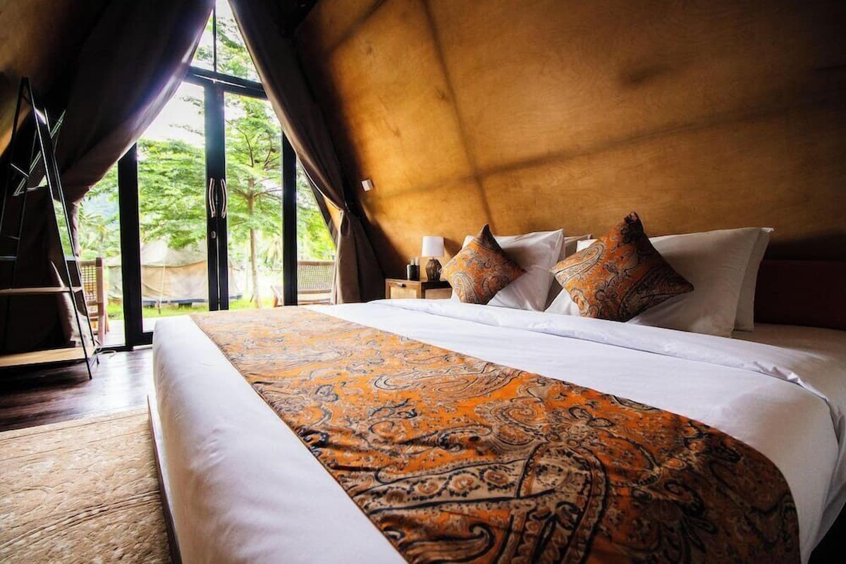 A bedroom with a large bed, a window, and a view of greenery outside.