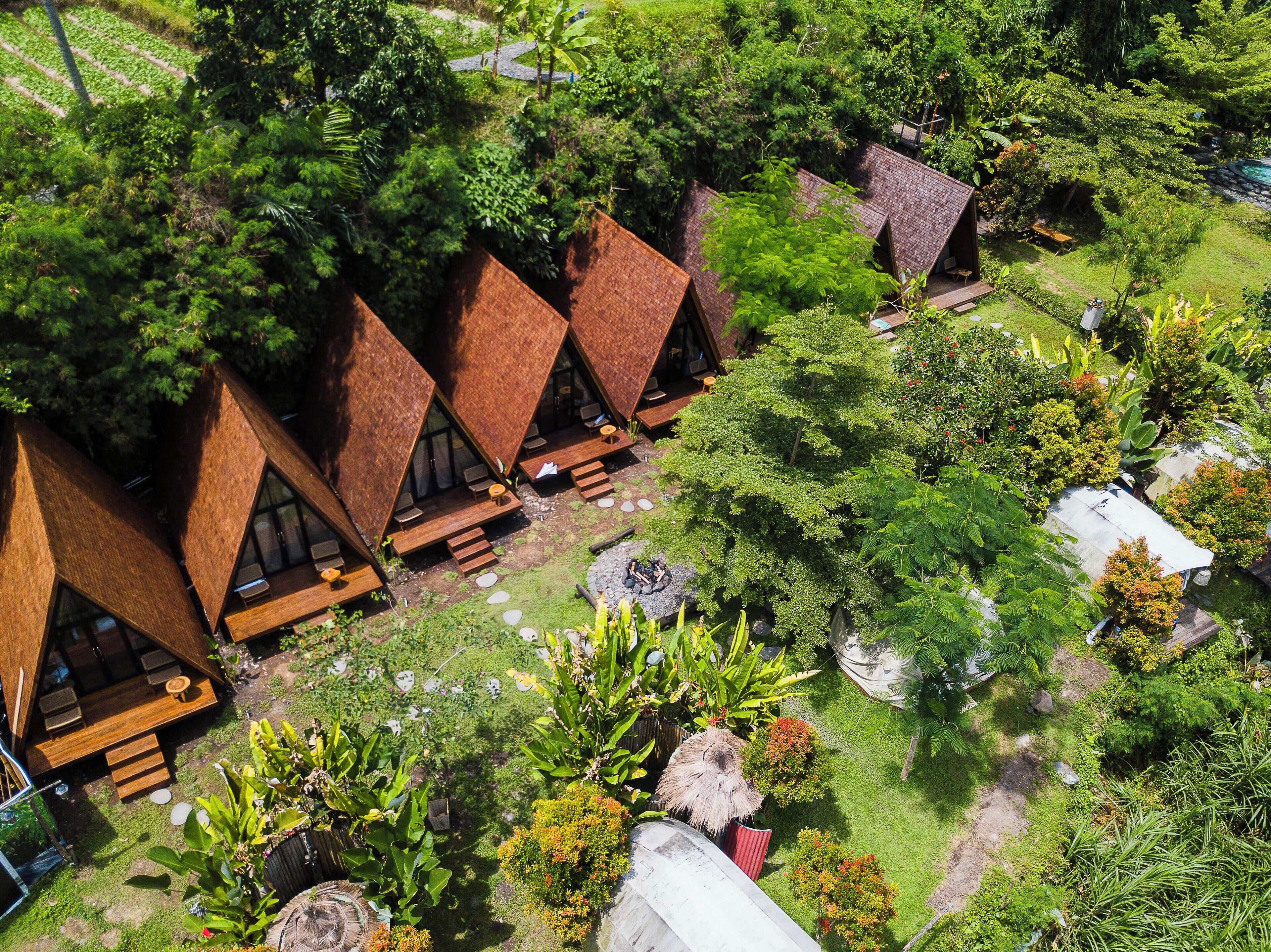 A series of triangular-roofed cabins with outdoor seating areas, surrounded by lush greenery and a small pond.