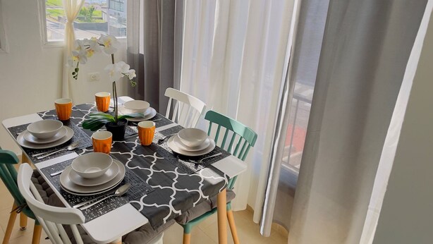 A dining area with a table set for four, chairs, and a view of the ocean through sheer curtains. - Apartment on the beach, new (Bat Yam)