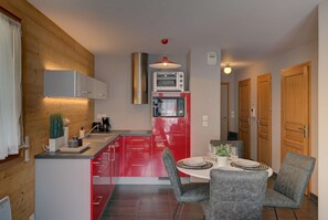 Une cuisine de taille réduite, avec un réfrigérateur rouge, un four encastré et une machine à café.
