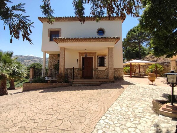 A two-story house with a stone facade, a tiled roof, and a paved entrance area. - Stunning villa in Ronda with a private pool and barbecue. (Ronda)