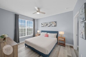 A bedroom with a bed, two bedside tables, a ceiling fan, a window with curtains, and artwork on the wall. - 3176-301 Resort 2BR Apt by Disney World Orlando (Kissimmee)