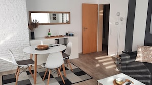 A modern living room with a dining area, a sofa with patterned cushions, a coffee table, and a large window with a view of a bridge.