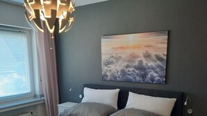 A bedroom with a large bed, a wall-mounted painting, a bedside table, and a modern pendant light.