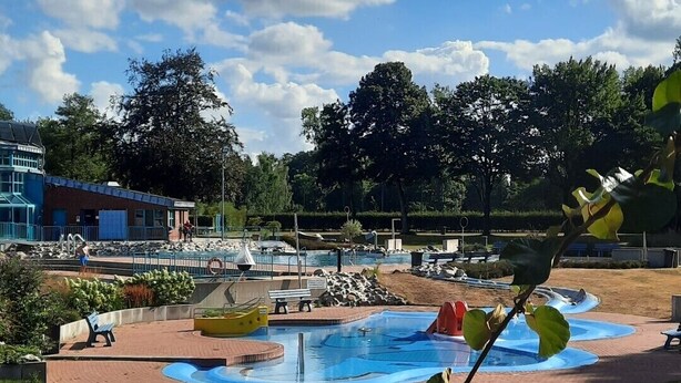 A park with a swimming pool, benches, and a building in the background.