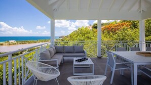 A covered outdoor seating area with a view of the ocean and greenery. - Villa Angelsmart – Contemporary Sea View Villa Overlooking Red Bay, St. Maarten (Phillsburg)