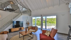 A spacious living area with a large TV, comfortable seating, and a balcony with a view. - Villa Angelsmart – Contemporary Sea View Villa Overlooking Red Bay, St. Maarten (Phillsburg)