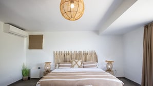 A modern bedroom with a large bed, a woven ceiling light, and a bedside table with a lamp. - Villa Angelsmart – Contemporary Sea View Villa Overlooking Red Bay, St. Maarten (Phillsburg)