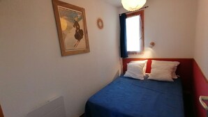 Et lille, pænt indrettet soveværelse med en enkeltseng, en radiator, et indrammet plakat på væggen og et vindue med gardiner.