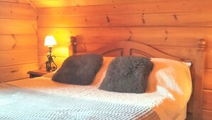 A wooden cabin bedroom with a bed, two pillows, a nightstand with a lamp, and a wooden headboard. - Chalet in La Joue du Loup, sleeps 6, terrace, parking (La Joue du Loup)