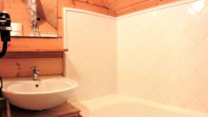 A bathroom with a white sink, a bathtub, and wooden paneling. - Chalet in La Joue du Loup, sleeps 6, terrace, parking (La Joue du Loup)
