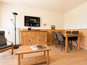 A modern living room with a wooden table, a sofa, a TV mounted on the wall displaying a Netflix interface, and a framed picture on the wall.