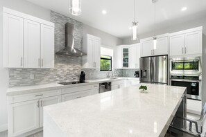 A modern kitchen with white cabinets, stainless steel appliances, a large island, and pendant lighting.