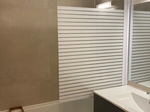 Un baño con un lavamanos blanco, un espejo y un separador de vidrio.