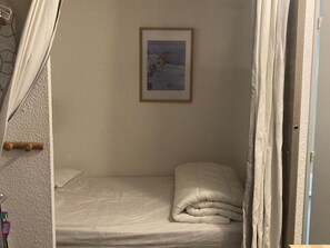 Una habitación pequeña con cama individual, una colcha blanca y un cuadro en la pared.