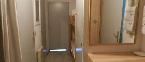 Un couloir étroit avec un plancher en bois, une porte au fond et un miroir au mur.