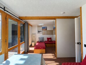 A compact room with a bed, a small table, and a sliding door leading to another room.