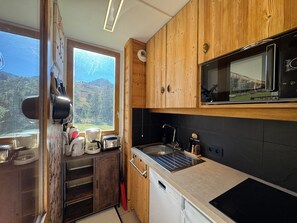 A compact kitchen with wooden cabinets, a built-in microwave, and a window overlooking a mountainous landscape.