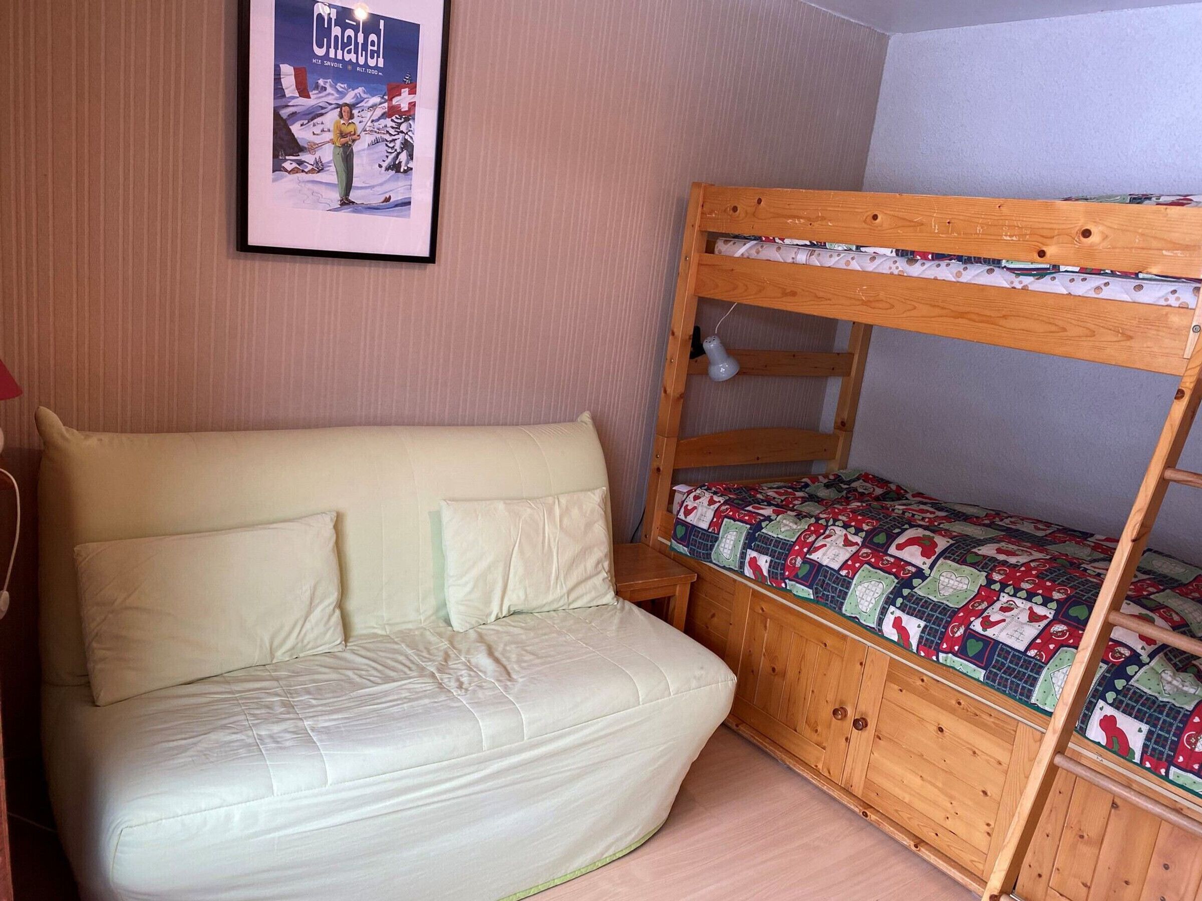 A bunk bed with a colorful quilt, a sofa with pillows, and a framed picture on the wall.