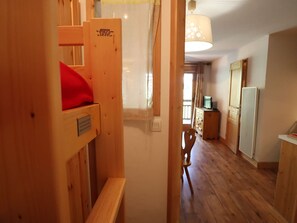 A wooden interior with a bunk bed, a bench, a wooden chair, a desk, and a refrigerator.