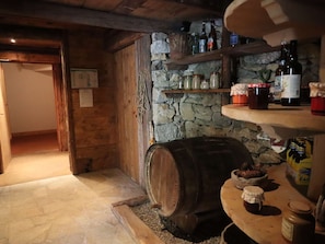 Um quarto rústico com paredes de pedra, vigas de madeira, um barril, prateleiras com garrafas e potes.