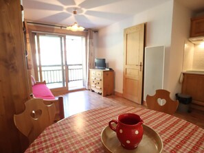 A room with a round table, a red polka-dotted pitcher on a tray, wooden chairs, a television on a cabinet, and a door.