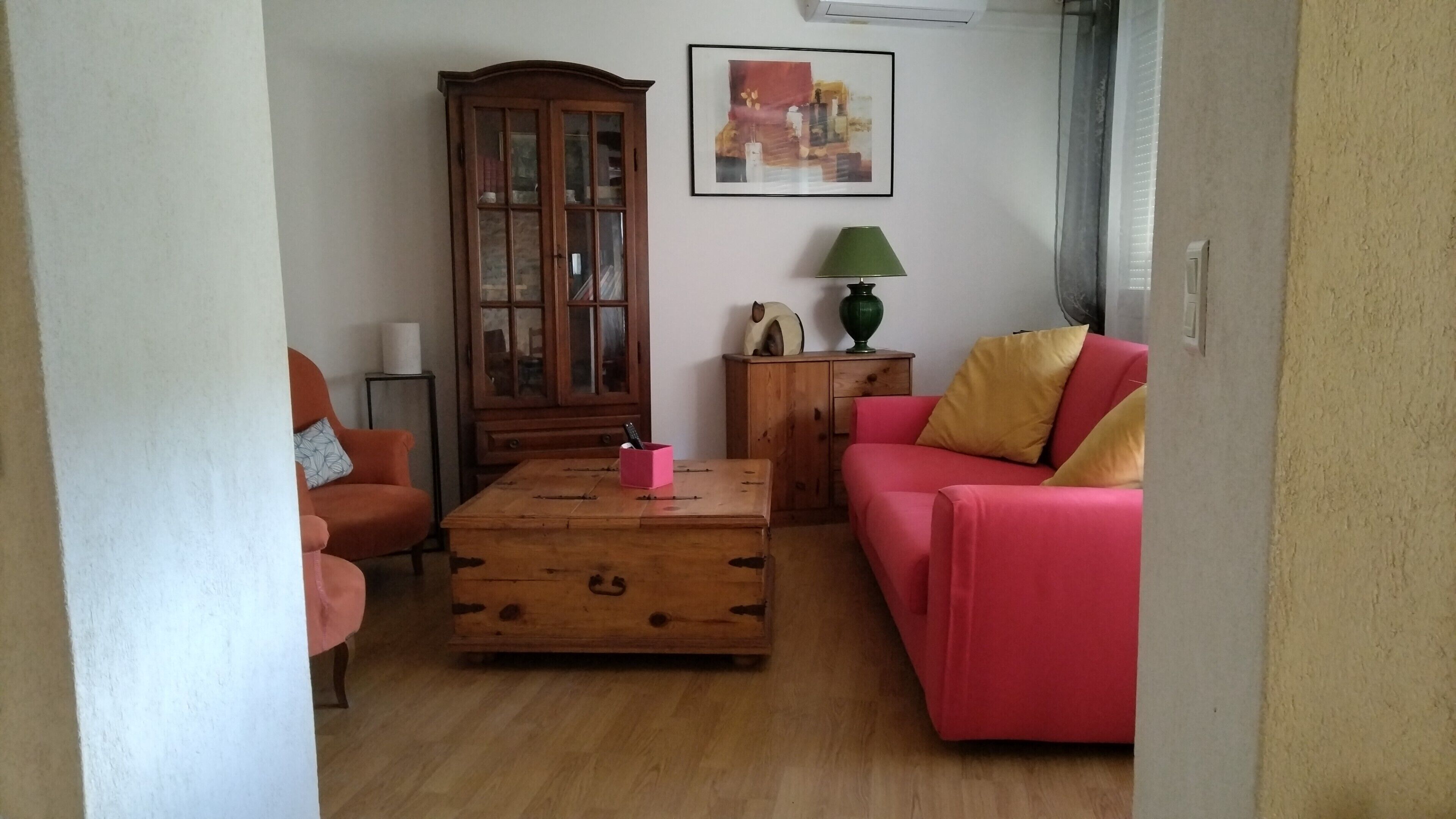 A living room with a wooden coffee table, a red sofa, a wooden cabinet, and a painting on the wall.