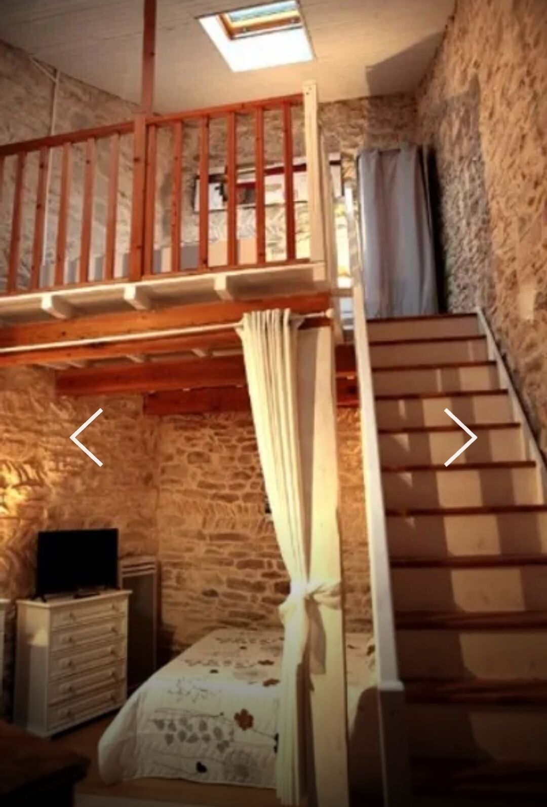 A rustic room with a loft bed, a staircase, and a stone wall.