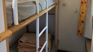 A bunk bed with a wooden frame and white metal railings, a small shelf below, and a curtain with a floral pattern on the adjacent wall. - Functional studio 3/4 pers with balcony and direct slopes access (Belle Plagne)