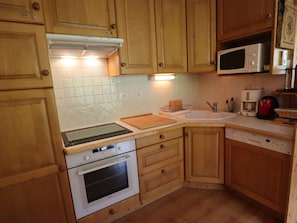 A compact kitchen with wooden cabinets, a microwave, a stove, and a sink.